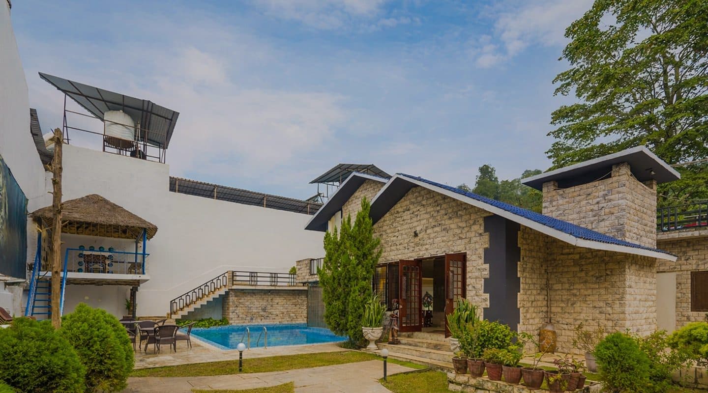 Amaltas Villa's stone cottage and swimming pool among trees